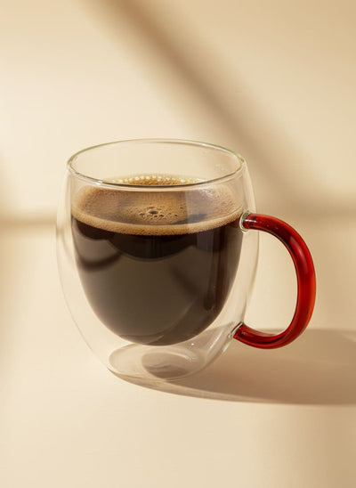 Insulated double-wall glass coffee mug with a vibrant red handle, filled with black coffee.