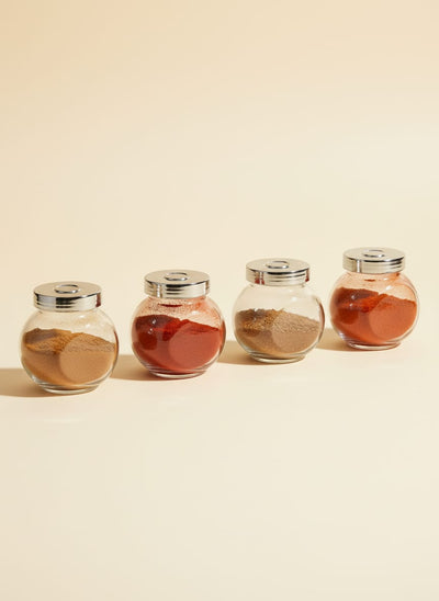 Set of four round glass spice jars with silver lids, lined up against a white background.