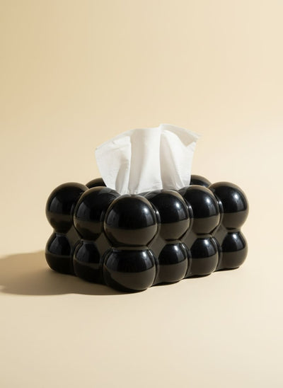 Modern black bubble tissue box holder with a white tissue, on a white reflective surface.